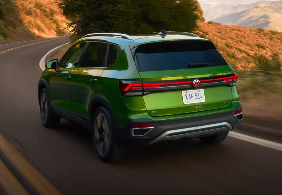 Green Volkswagen Taos driving along a winding mountain road, shown in a rear three-quarter view.