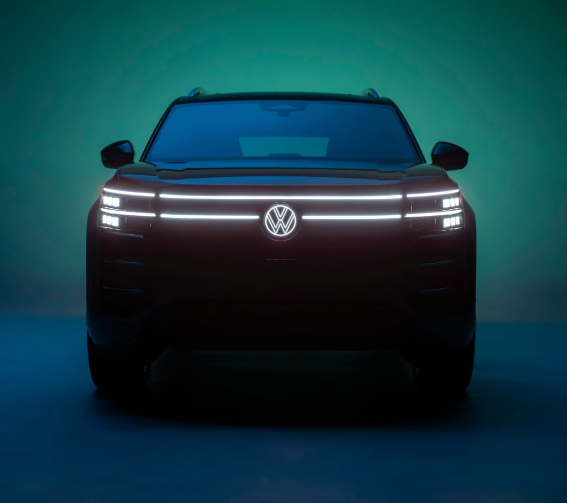 Front view of a Volkswagen Atlas with illuminated LED headlights and Volkswagen emblem against a dark teal background.